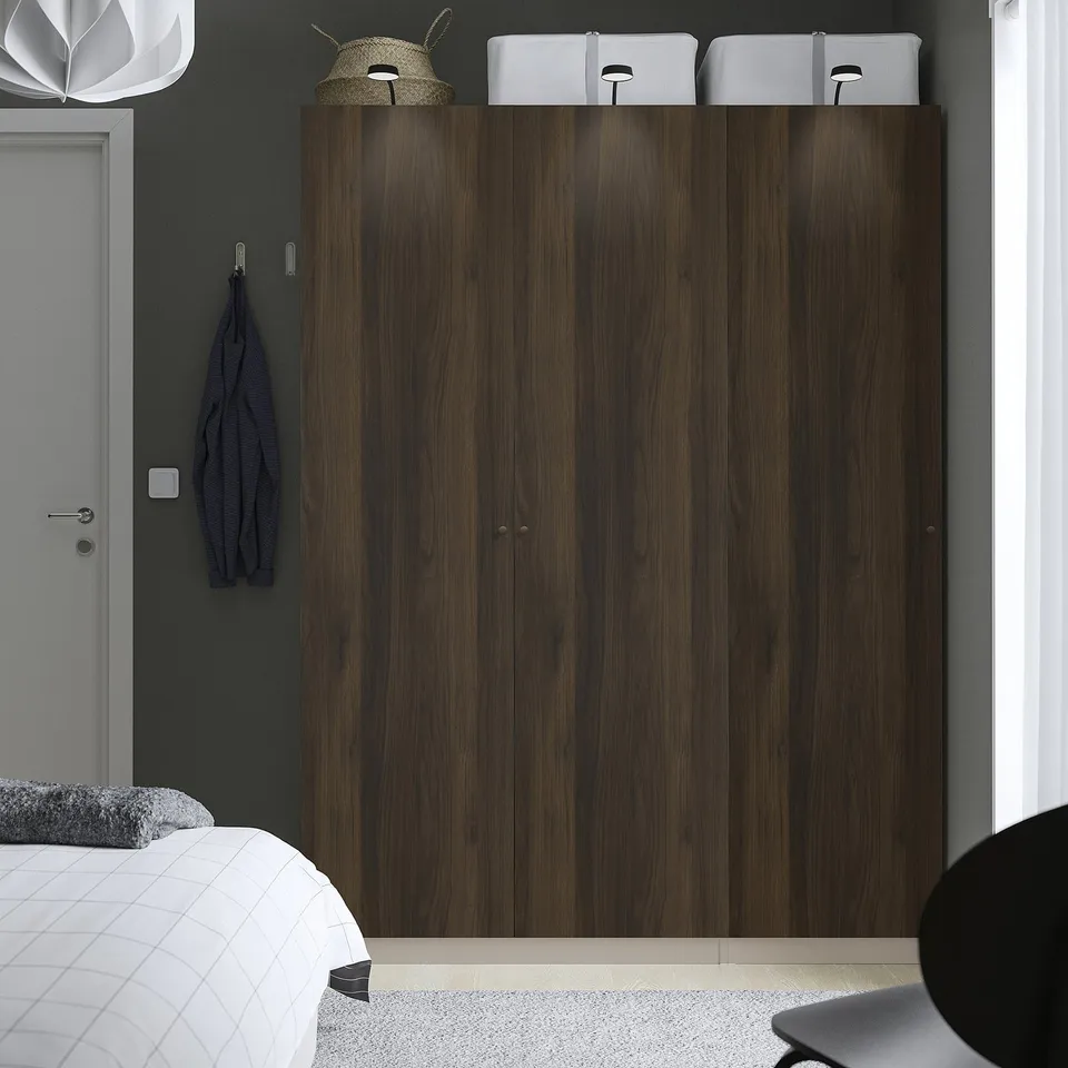 Modern bedroom with large dark wooden PAX wardrobe, white bed, wall hooks, and hanging hat.
