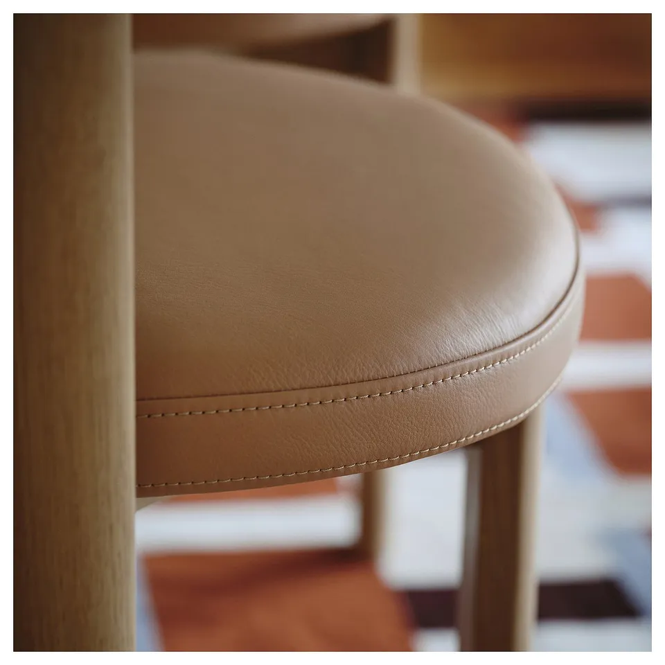 Close-up of smooth, stitched leather seat on elegant wooden chair, showcasing quality craftsmanship.