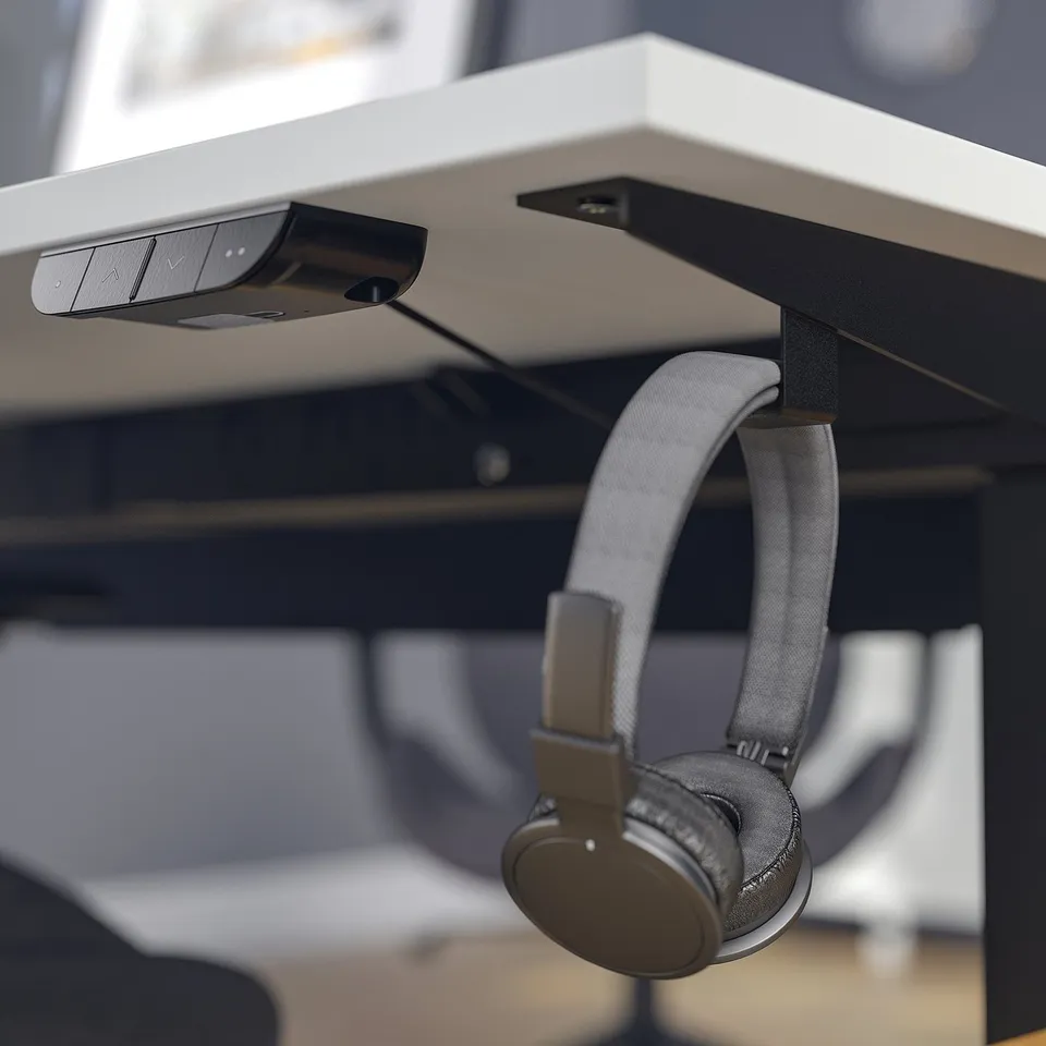 Headphones hang on desk hook above sit-stand control.