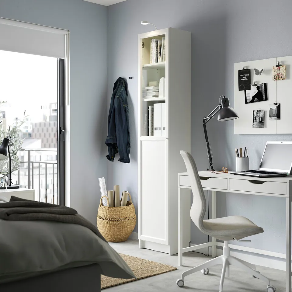 Modern home office with BILLY bookcase, desk, and grey chair. Bookcase has glass doors.