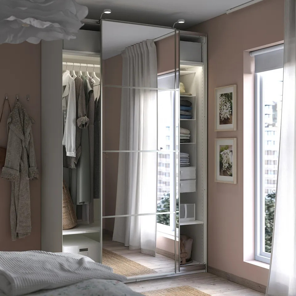 Modern bedroom with PAX mirrored wardrobe. Its creme-white, has sliding doors, and houses clothes, with a window beside it.