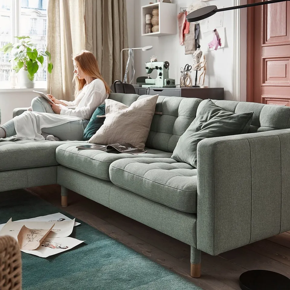 Person reads on green sofa with design tools.