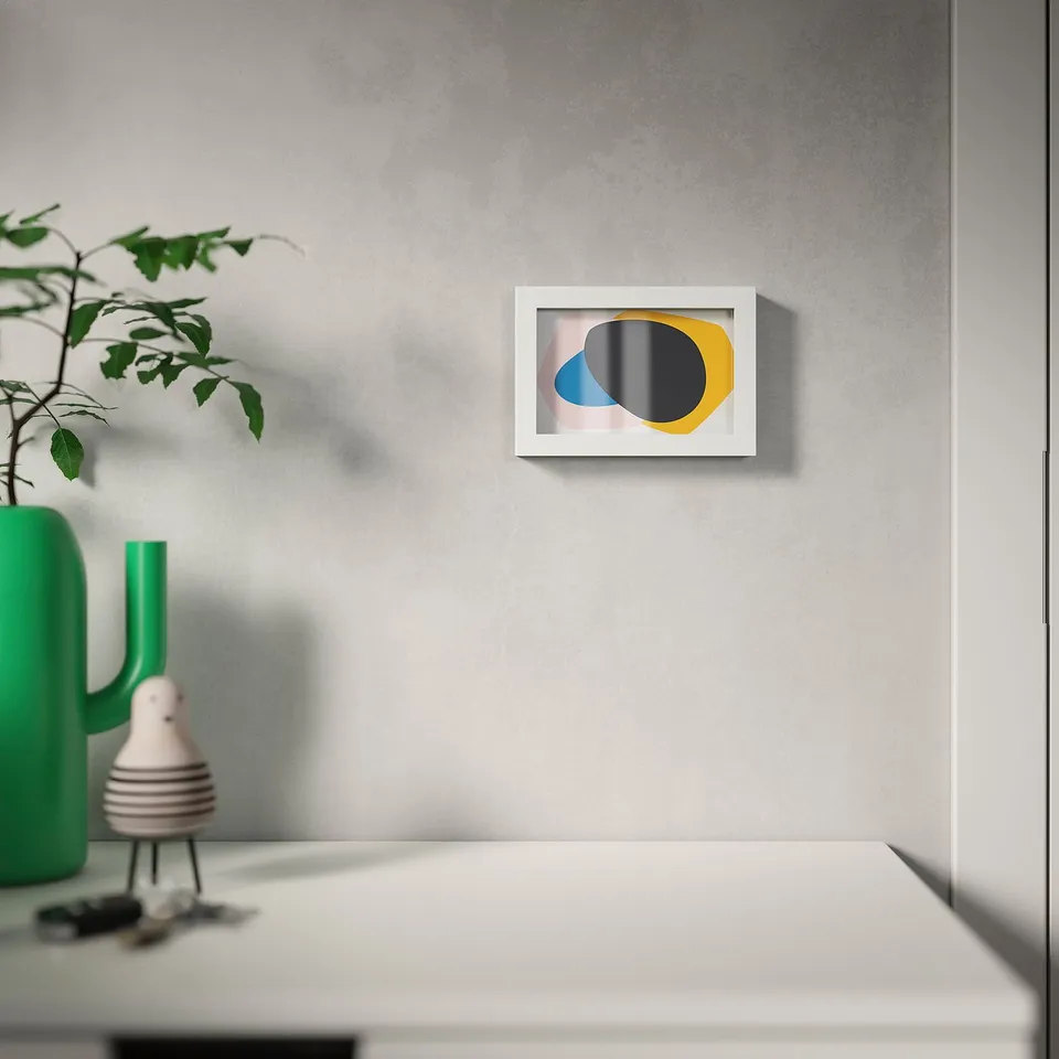 Modern frame on wall, holding abstract art in blue, yellow, and black. It stands on a table with a green vase and white figurine.