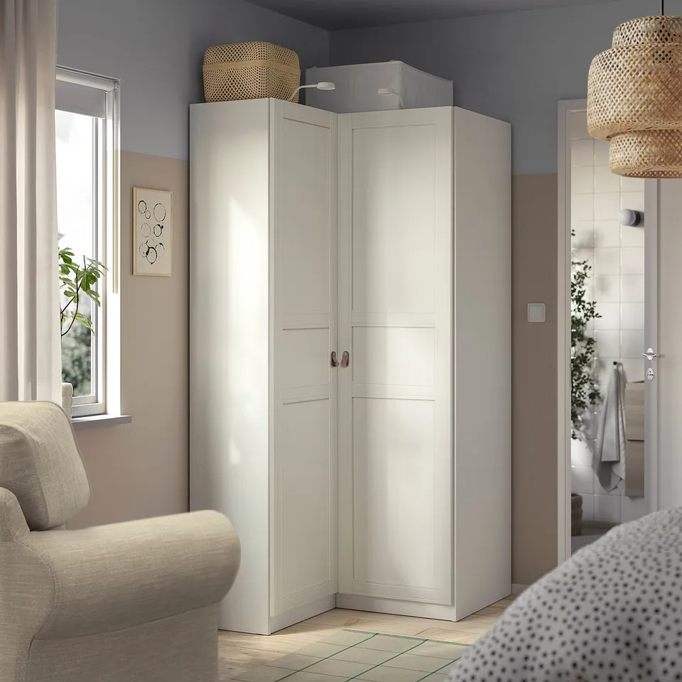 White PAX wardrobe in corner, taller than sofa, with basket and adjustable feet.