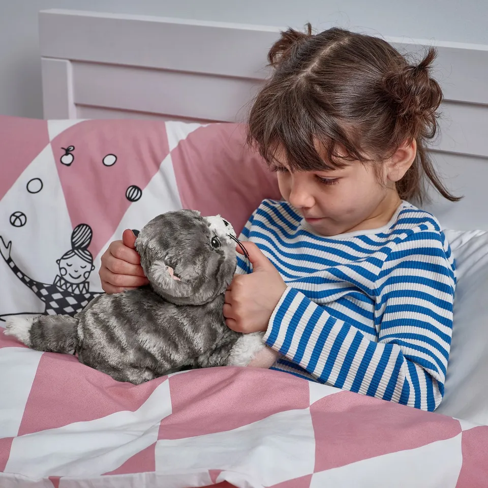 Young girl in striped pyjamas hugging a soft grey kitten toy in bed, illustrating the toys comforting and cuddly nature.