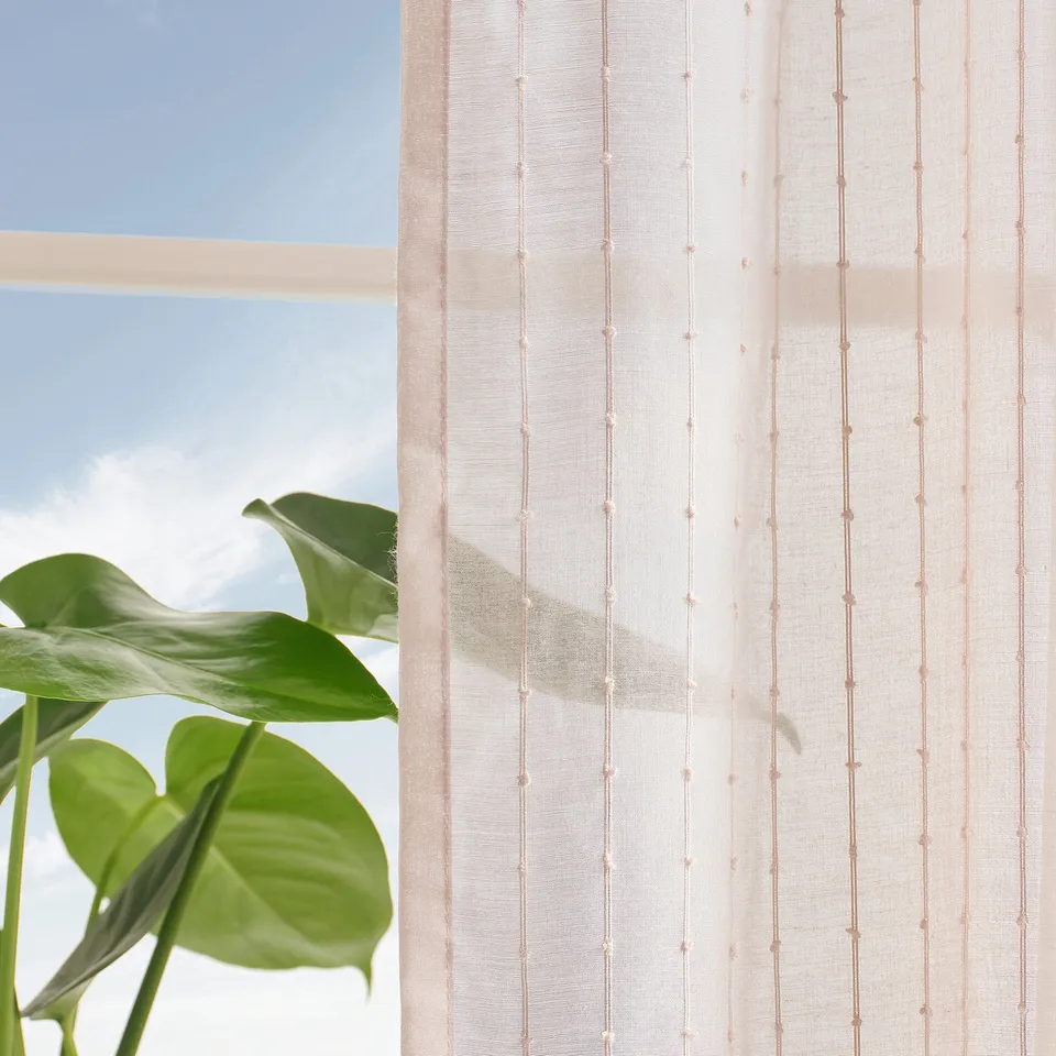 Sheer pink striped curtains with plant, softening light.