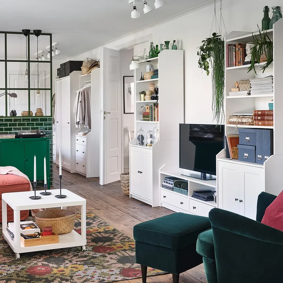 Bright living room with HAUGA white storage, green accents, red sofa, lush plants, and colourful rug. Tv stand, shelves with books and decor.