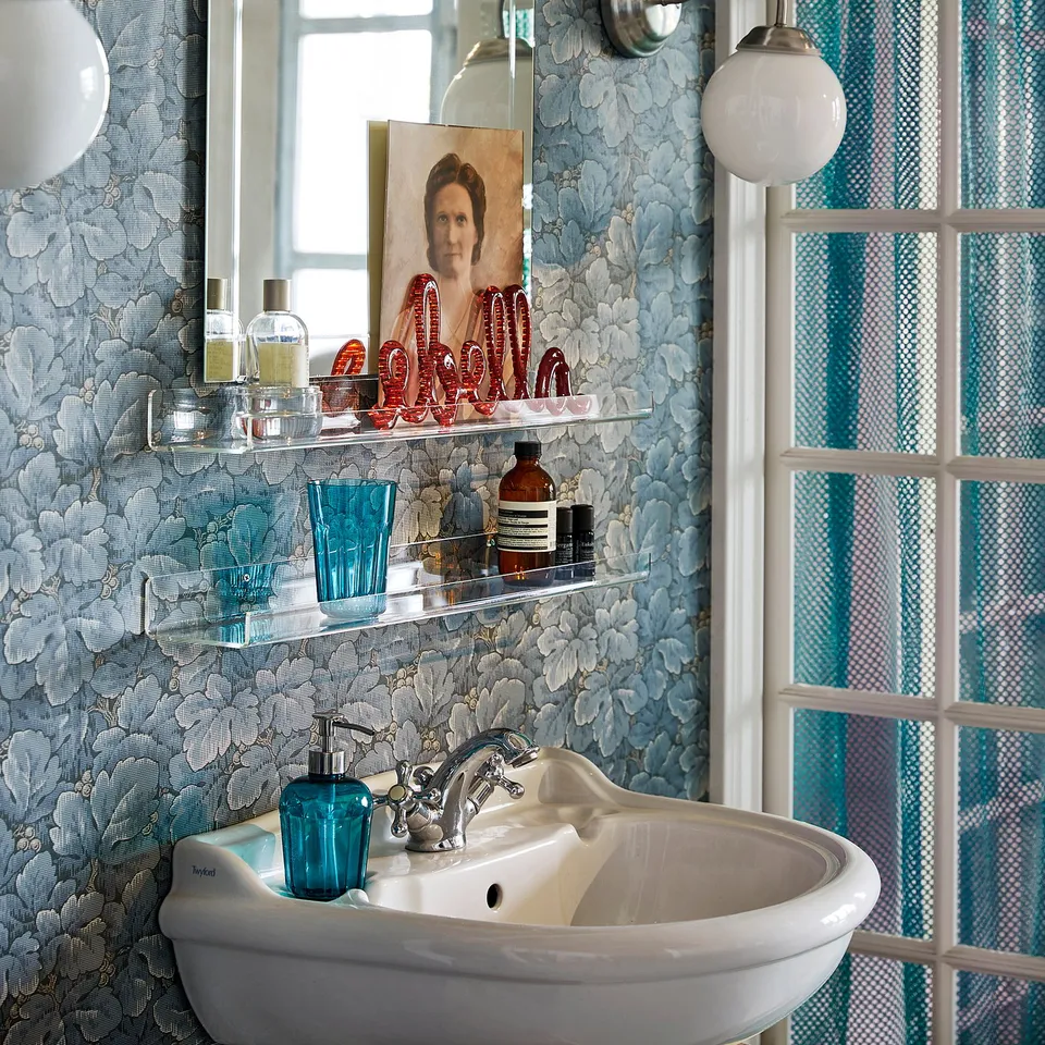 Alt: bathroom with MELLÖSA shelf, blue floral walls, white sink, and window with blue curtains.