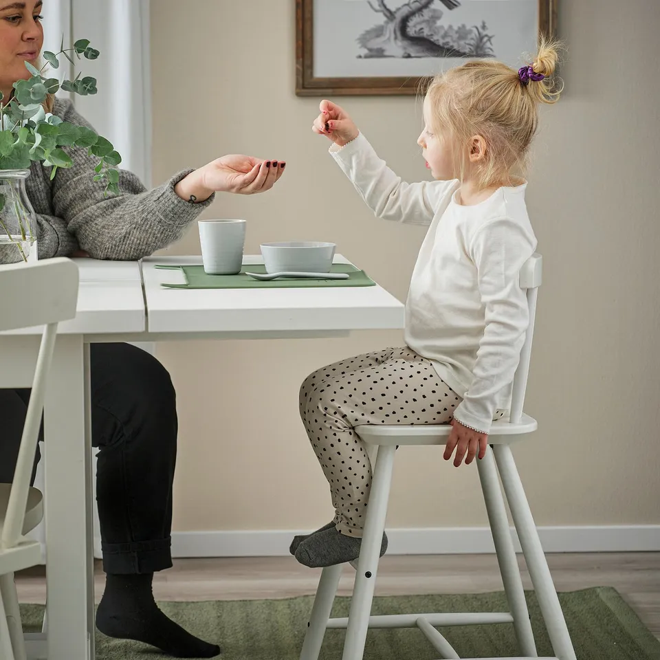 Child sits on a metal junior chair at a dining table, interacting with an adult.