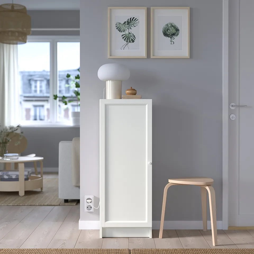 Minimalist room with BILLY white cabinet, blue wall, wooden stool, lamp, and botanical prints.