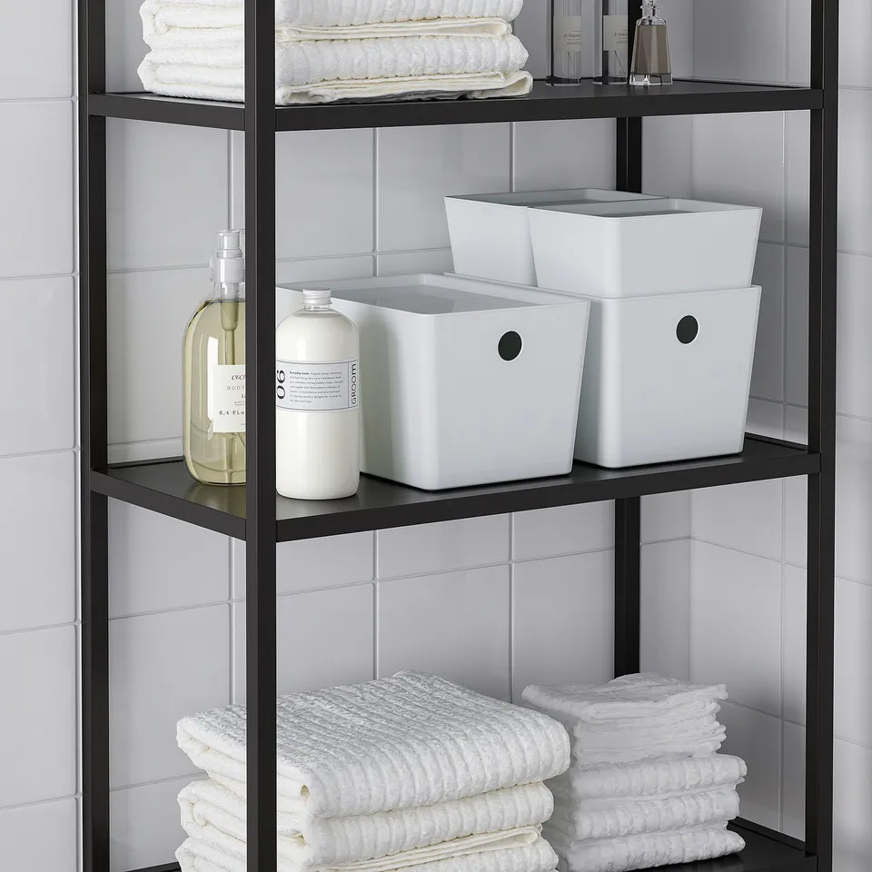 Black shelf with white towels, bottles, and KUGGIS boxes with lids.
