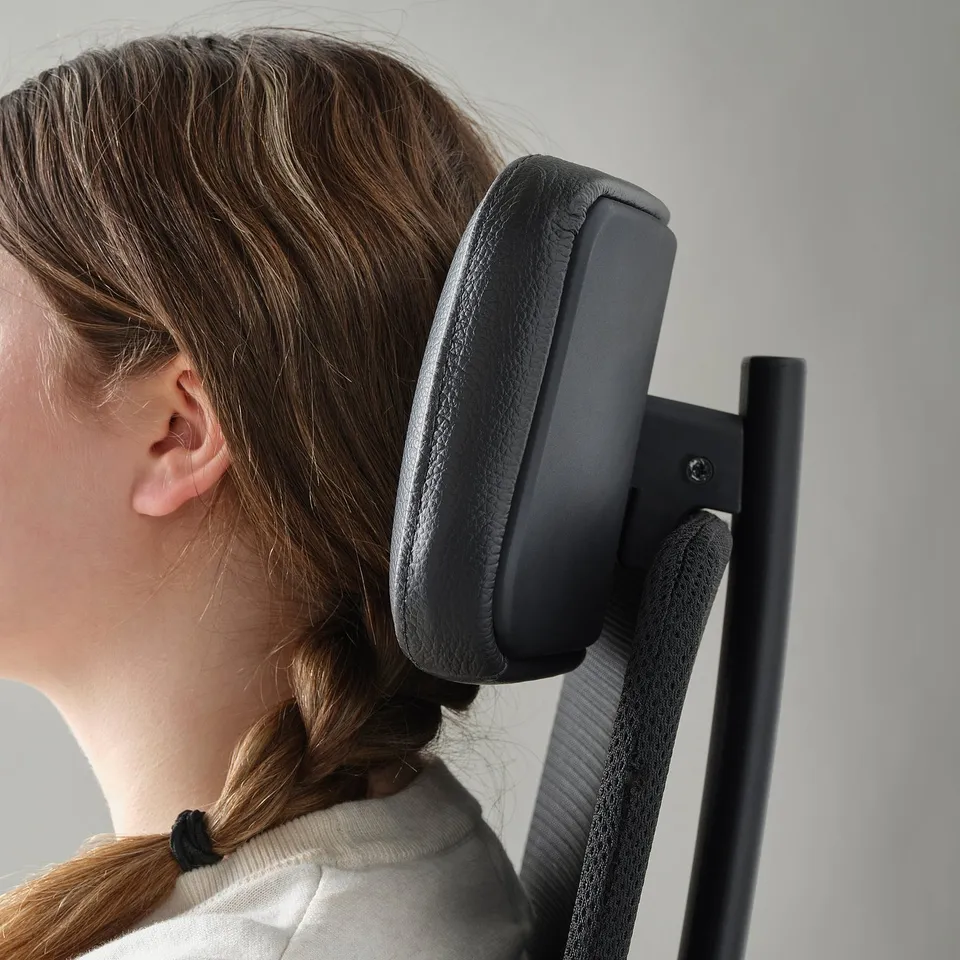 A person sitting in an ergonomic chair, leaning back on the adjustable headrest for support.