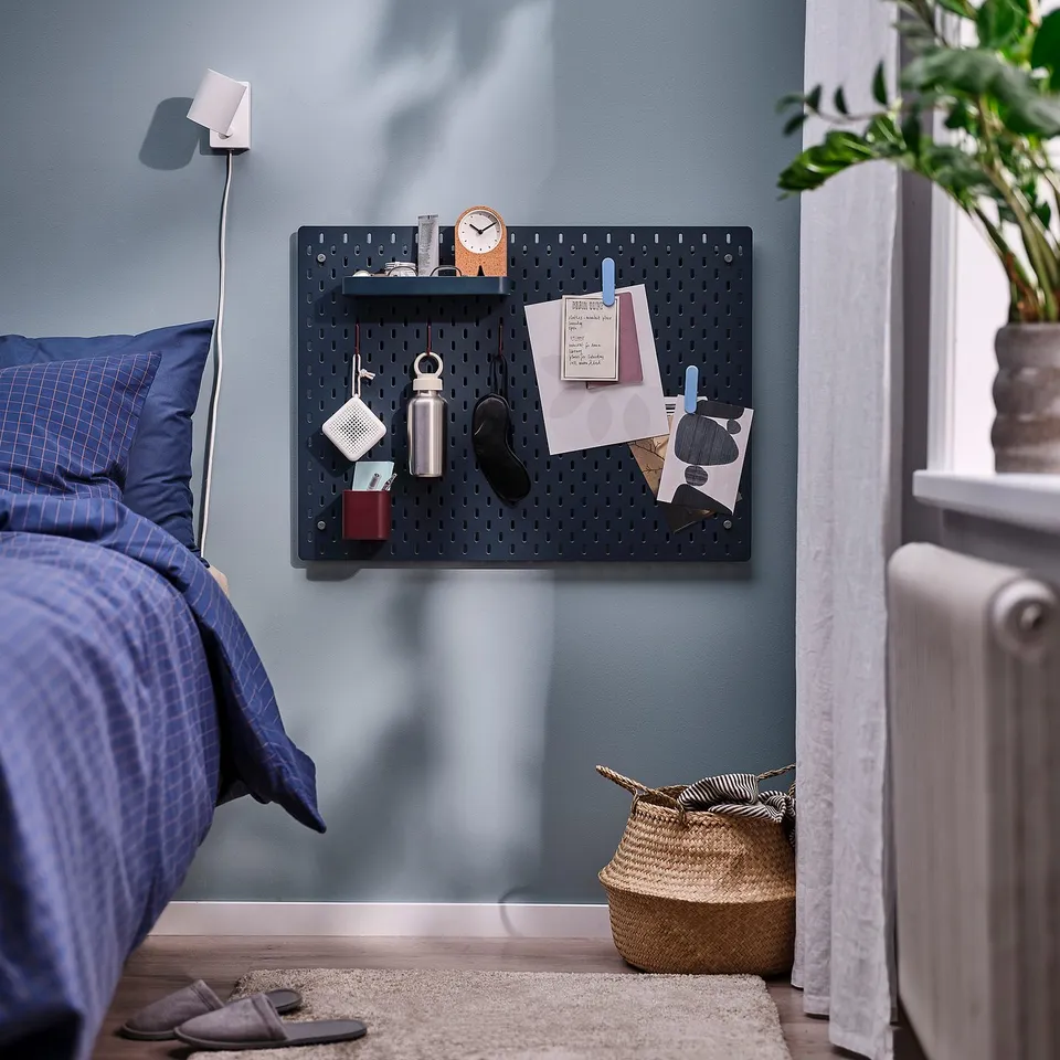 SKÅDIS pegboard with items, blue wall, bed, rug, basket.