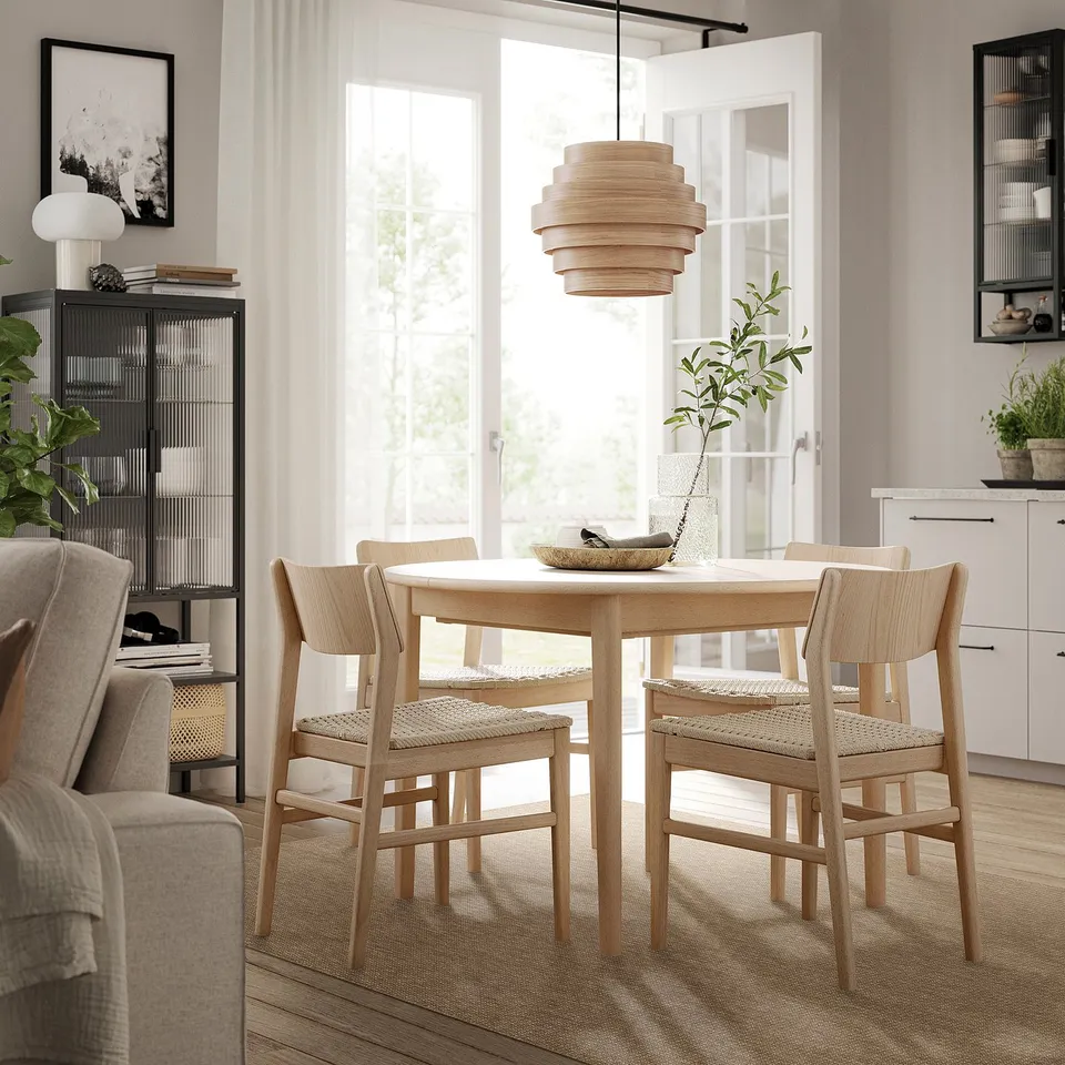 Modern dining room with LÄTTBETONG rug, table, chairs, and lamp. Surrounded by curtains, armchair, bookshelf, and plants.