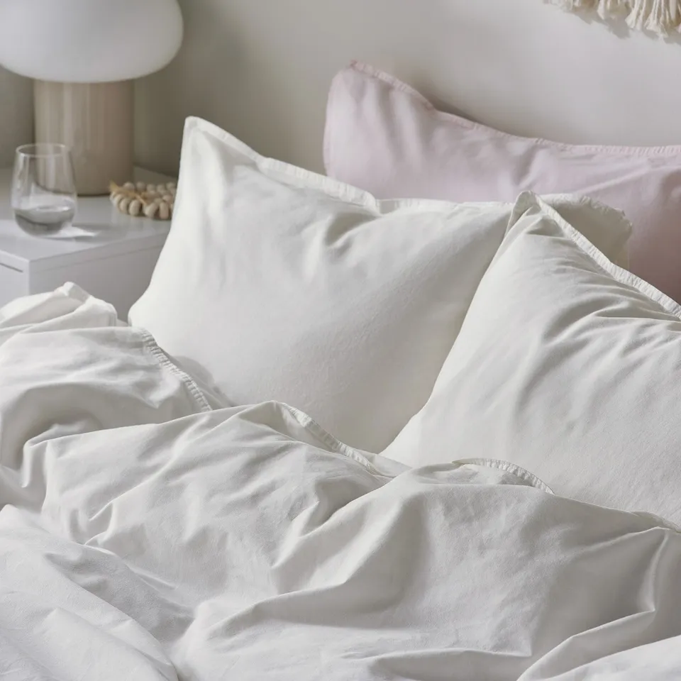 Image shows a neatly made bed with soft, white washed cotton sheets and pillows, exuding comfort and a casual, relaxed ambiance.