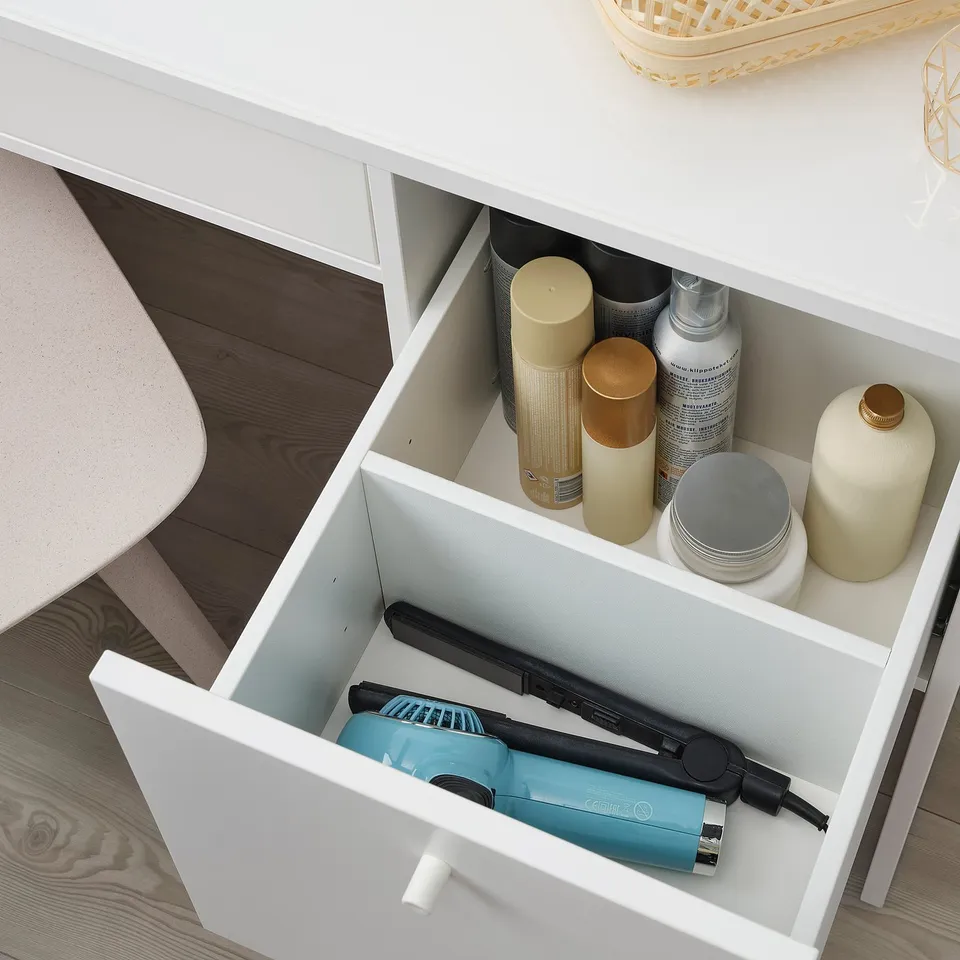 White vanity drawer open, revealing hair straightener, bottles, and containers neatly organised inside. Drawer divides items for easy access.