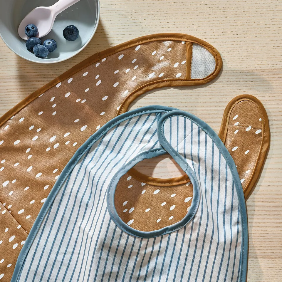 Two baby bibs - striped & dotted - on wood, with blueberries & spoon.