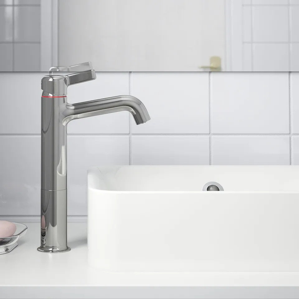 A chrome VOXNAN mixer tap saves water and energy with a cold-start function, shown in a modern bathroom sink setting.