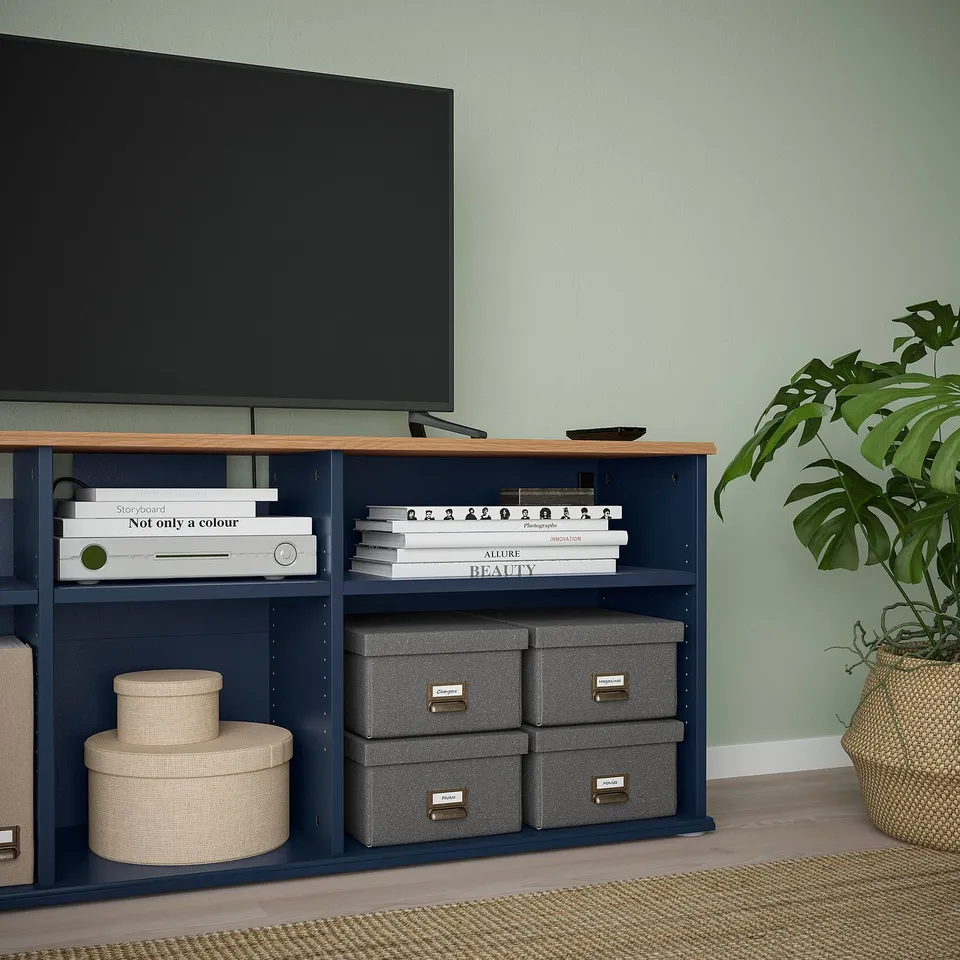 Modern tv unit with open shelves and storage boxes. Houses media devices, books, and a remote.