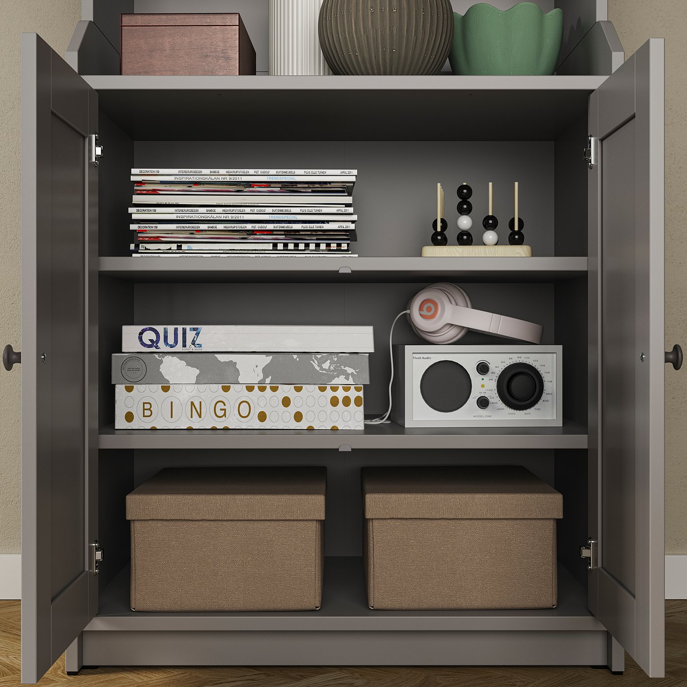 An open grey HAUGA storage cabinet with shelves holding books, board games, headphones, and decorative items.