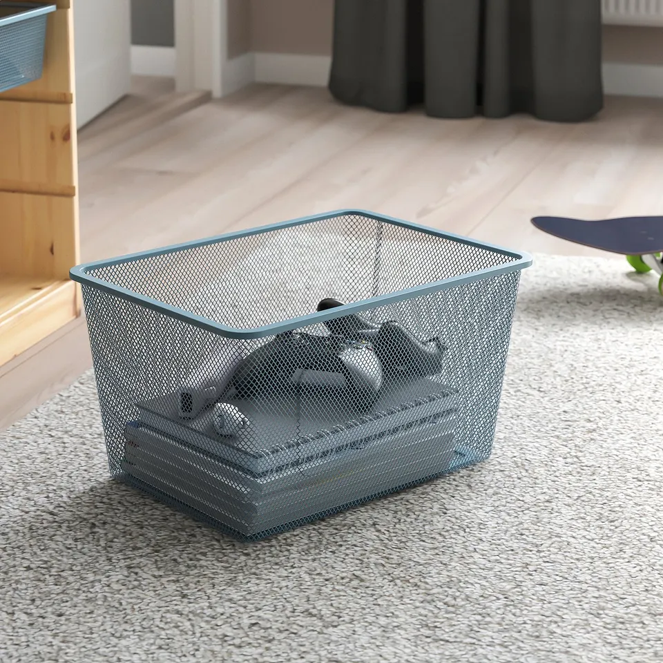 Mesh storage basket on floor, holding small items, part of TROFAST series for organising.