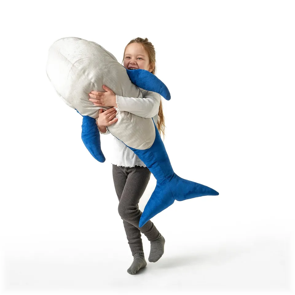 Girl cuddles large blue whale toy.
