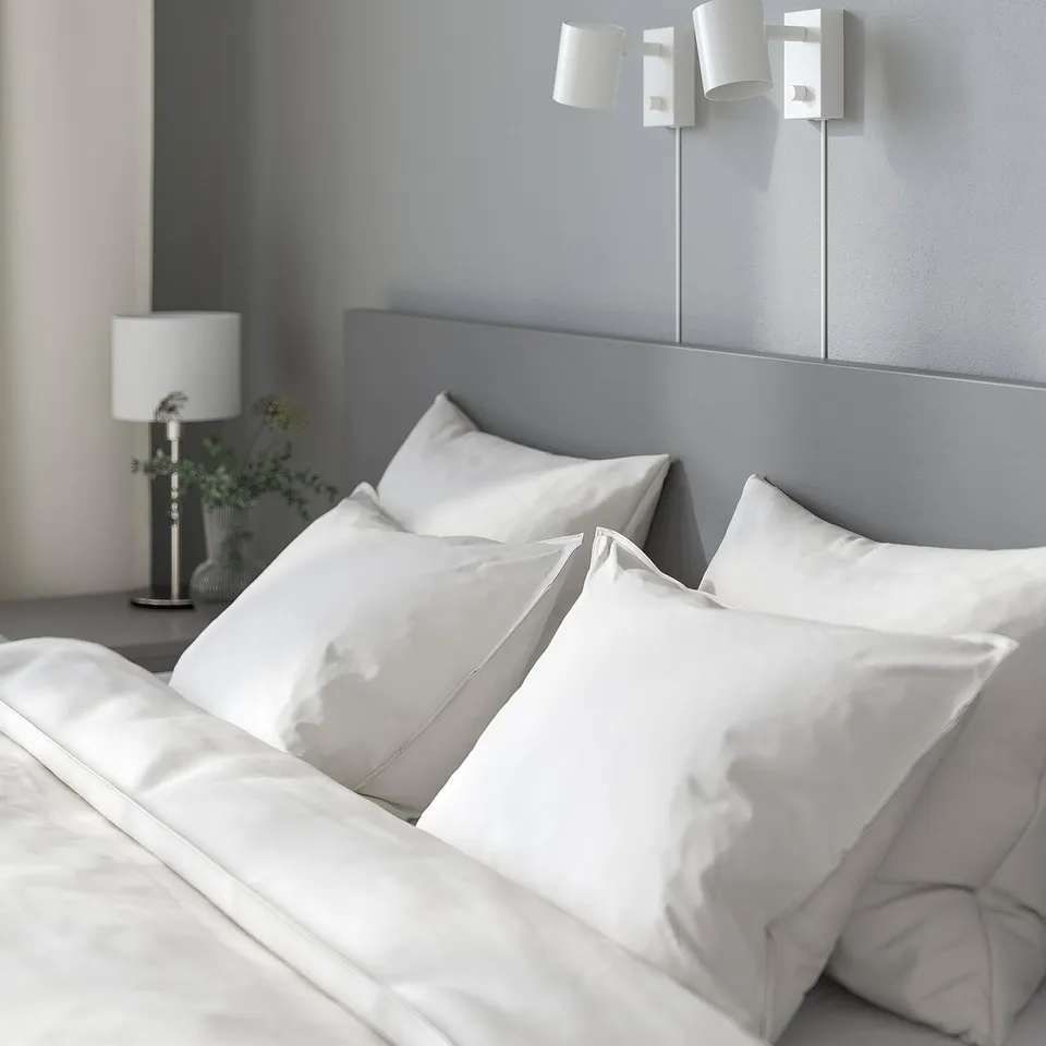 White bed with high, cushioned headboard and pillows, wall-mounted lights, and bedside lamp.