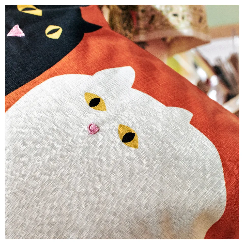 Adorable cat cushion, red, white, yellow. Hand-embroidered, cotton. Rounded design, playful cat face.