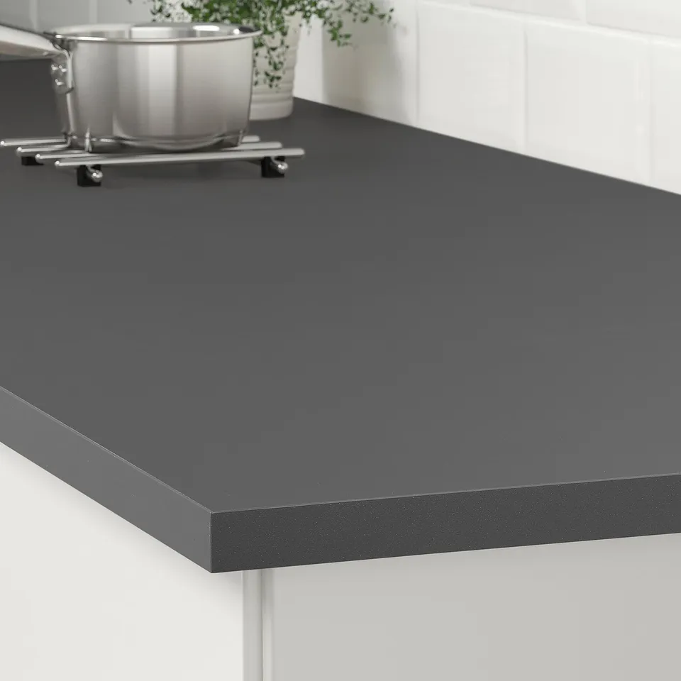 Black countertop with rounded edges. Stainless pots and plant. Easy to clean.