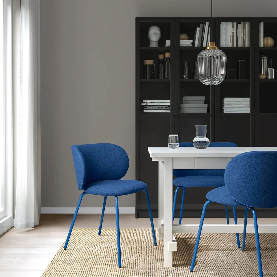 Modern dining area with blue KRYLBO chairs, grey table, black bookshelf, and hanging light.