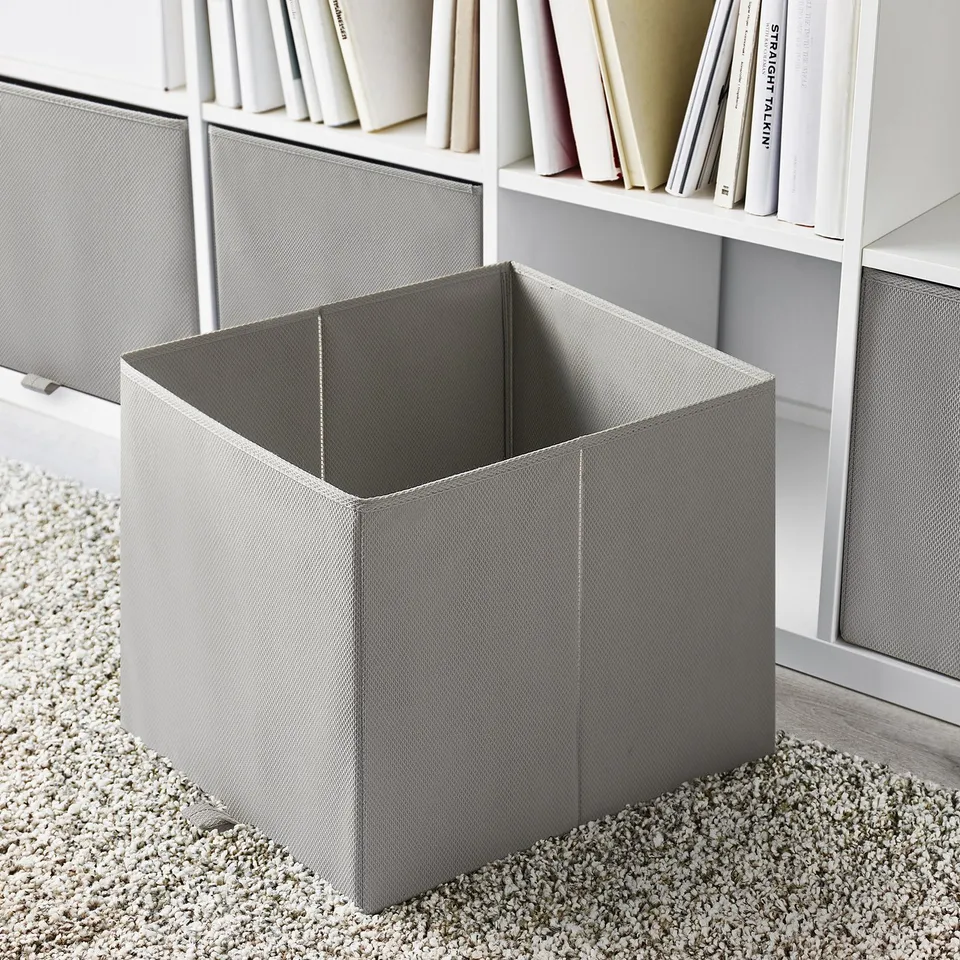 Empty grey storage cube, designed for kallax shelving, sits on textured carpet.