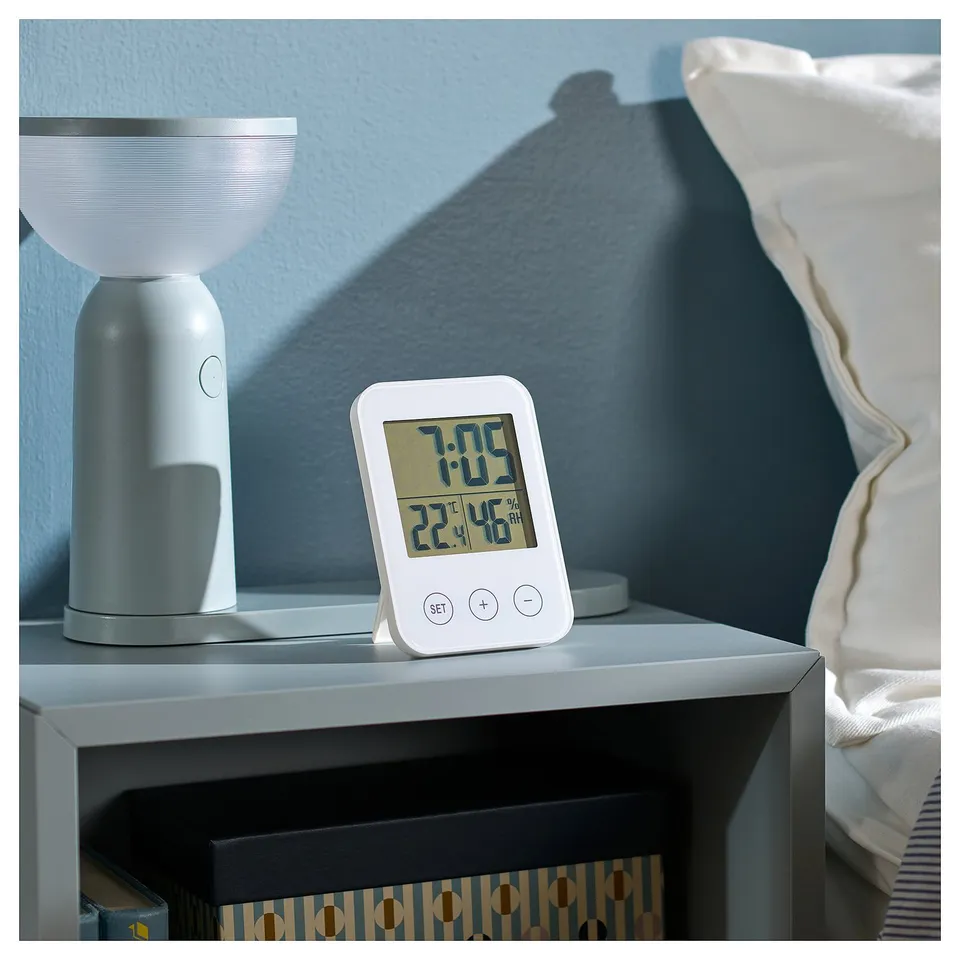 Bedside, white clock and lamp. Clock shows time, date, and humidity. Lamp modern, ribbed design.