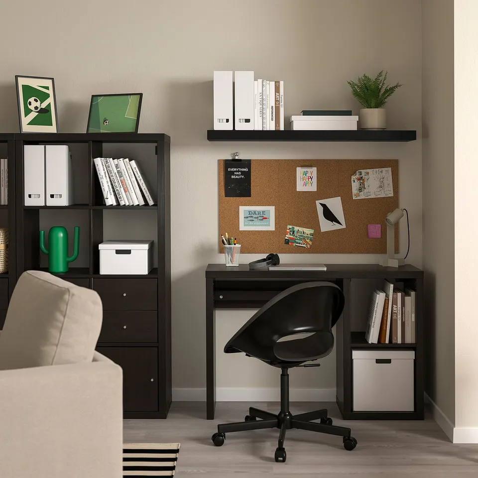 Home office with LACK wall shelf holding books, decor, and notes on corkboard above a beige sofa.