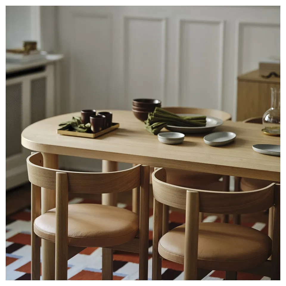 A modern dining set with a round oak table and four upholstered chairs. The table holds bowls and cups, ready for a meal.