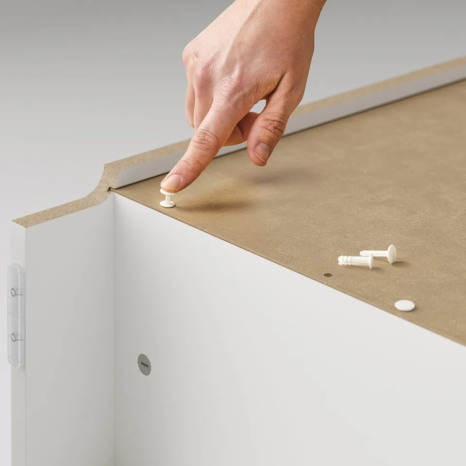 A person assembles a white BILLY bookcase, using plastic snap fittings on light brown shelves.