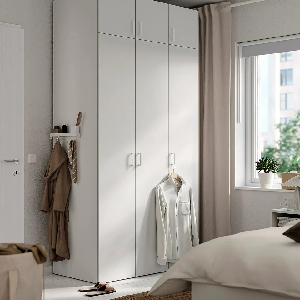 Modern LASTARE wardrobe tall with hanging clothes and shelves beside window.