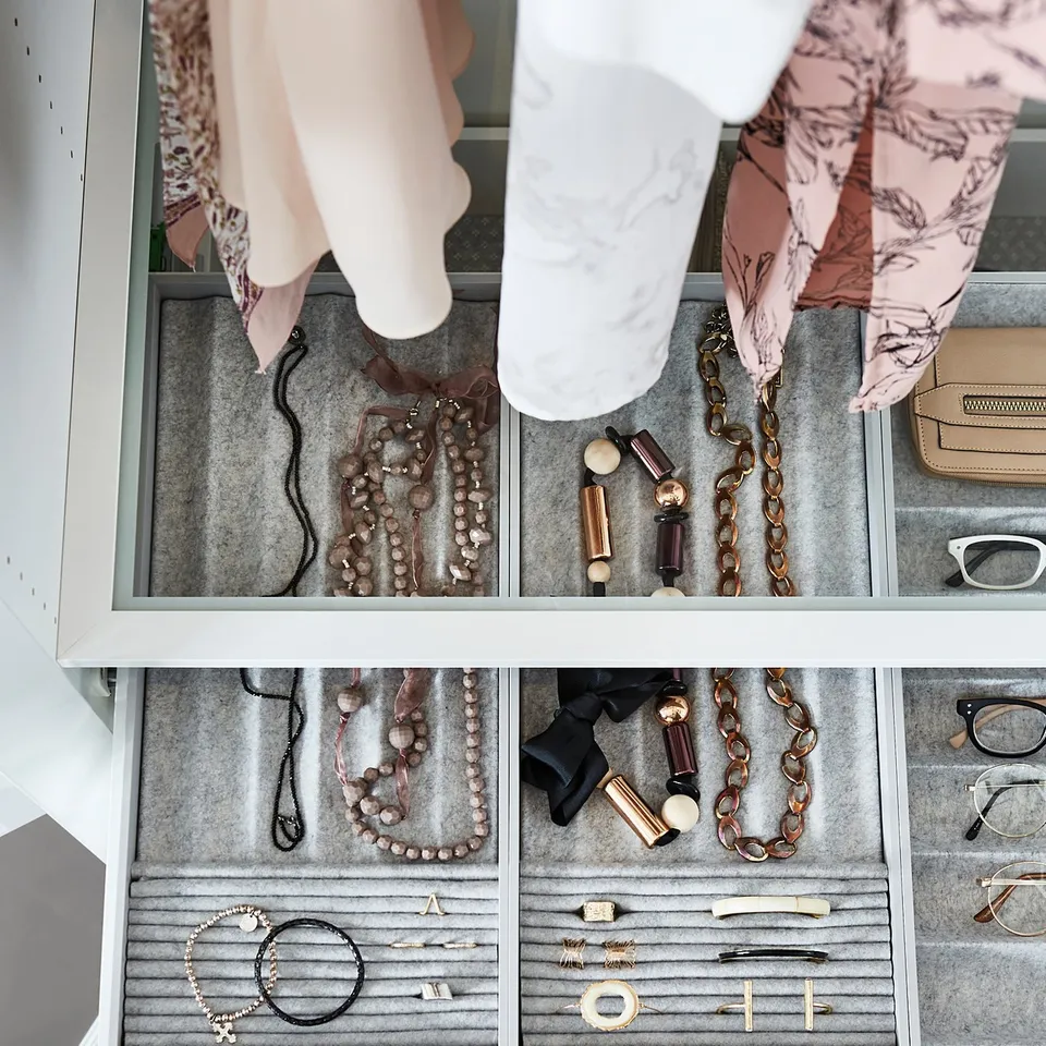 Person reaching into drawers of jewellery and accessories. Contains necklaces, bracelets, and rings on grey felt organisers.