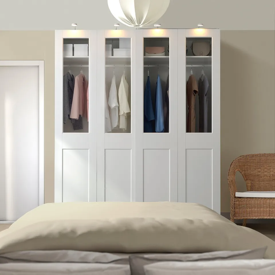White PAX wardrobe with colourful clothes, large bed & wicker chair.