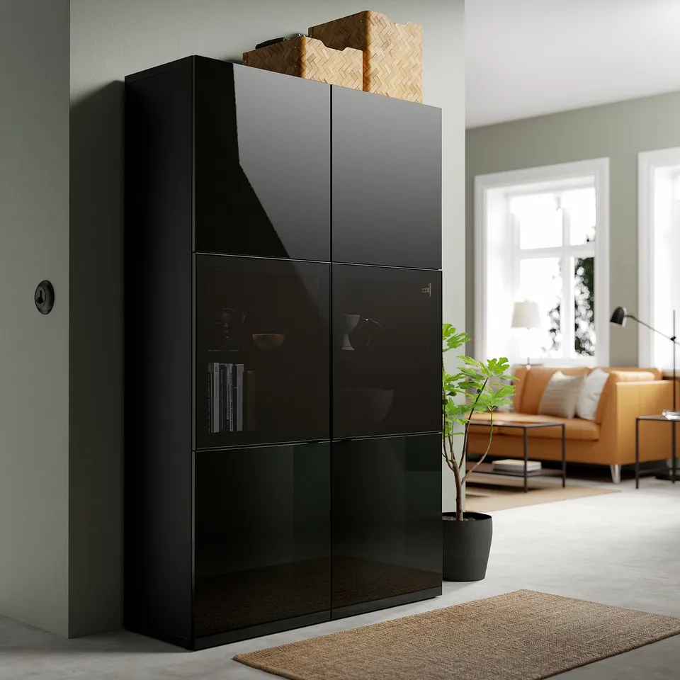 Black BESTÅ cabinet with glass doors items, stands tall near a cosy living area with a yellow couch and plants, providing ample storage.