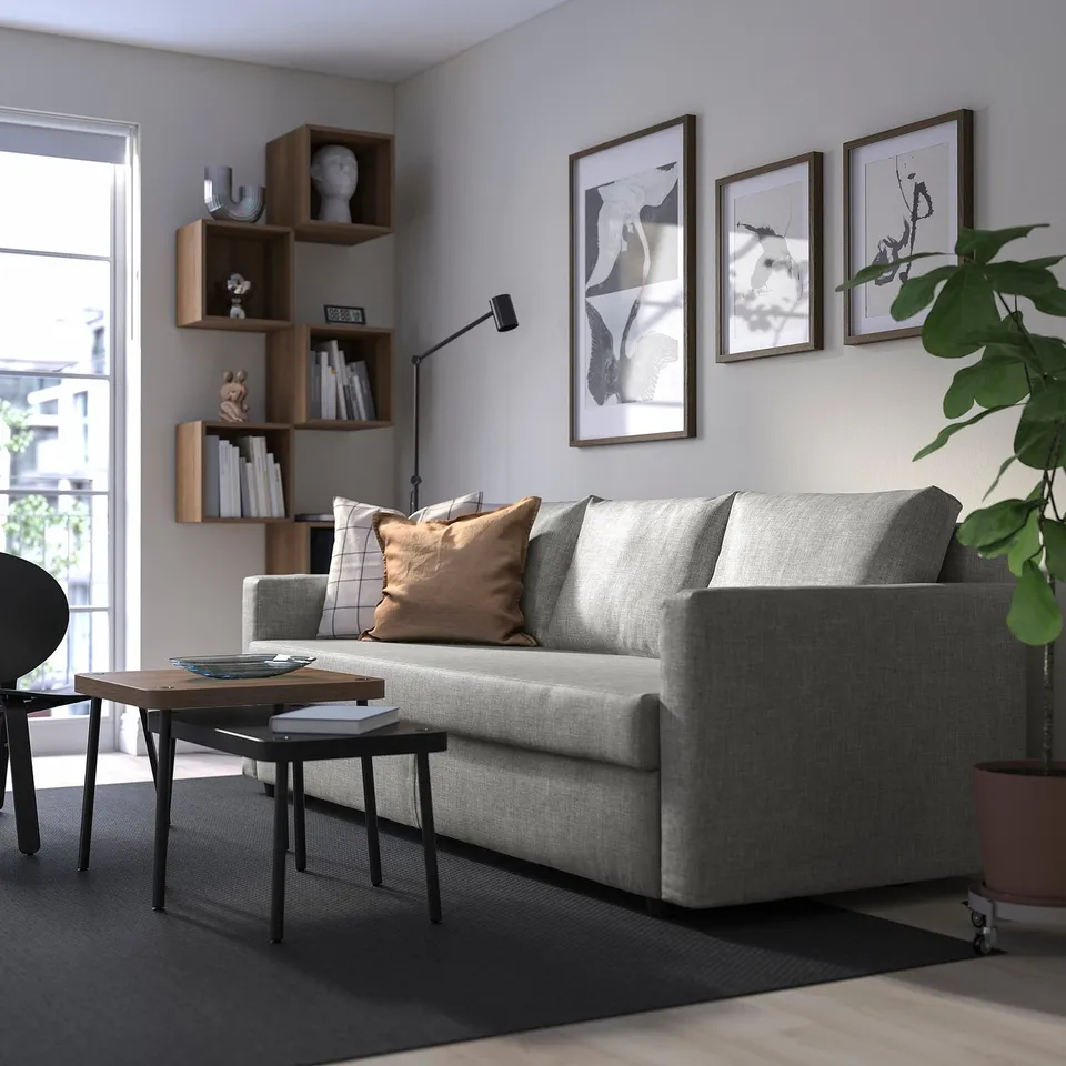 Grey FRIHETEN sofa, cushions, coffee table, bookshelf, art, plant, natural light.