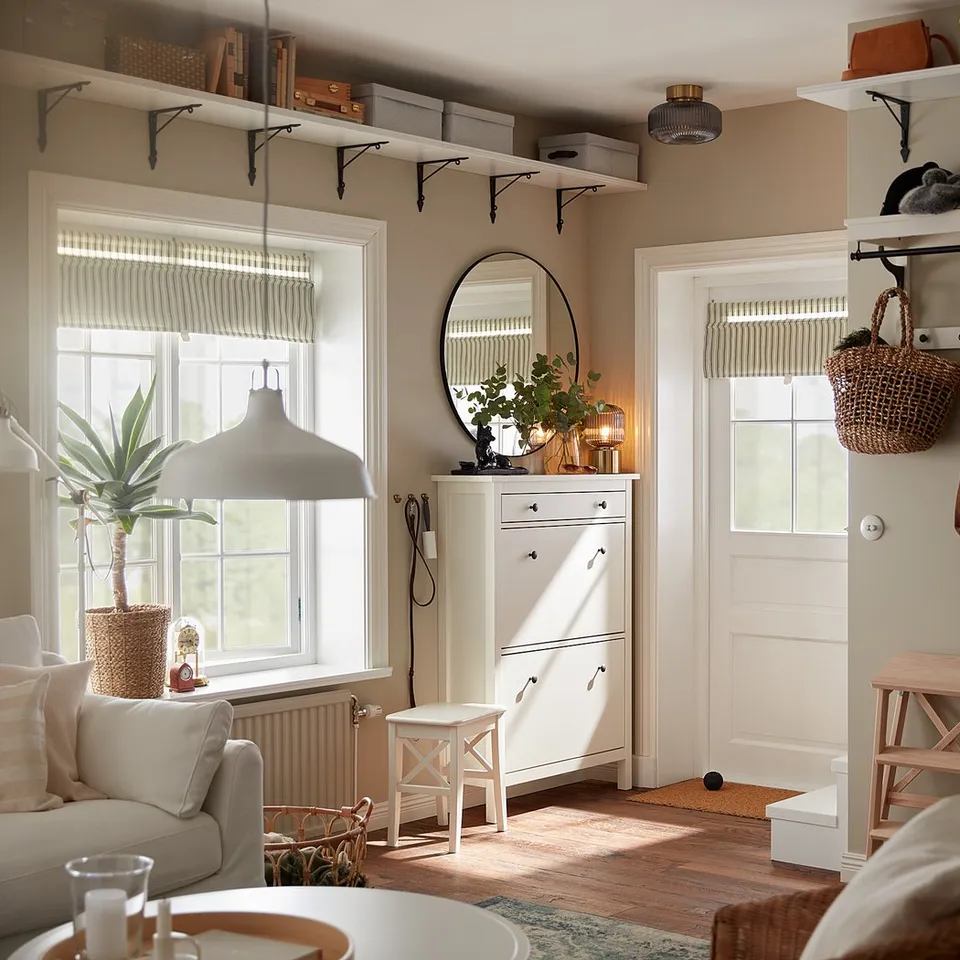 Room with BERGSHULT shelf, baskets, plants. Coats, bags by door, cabinet, stool under window.