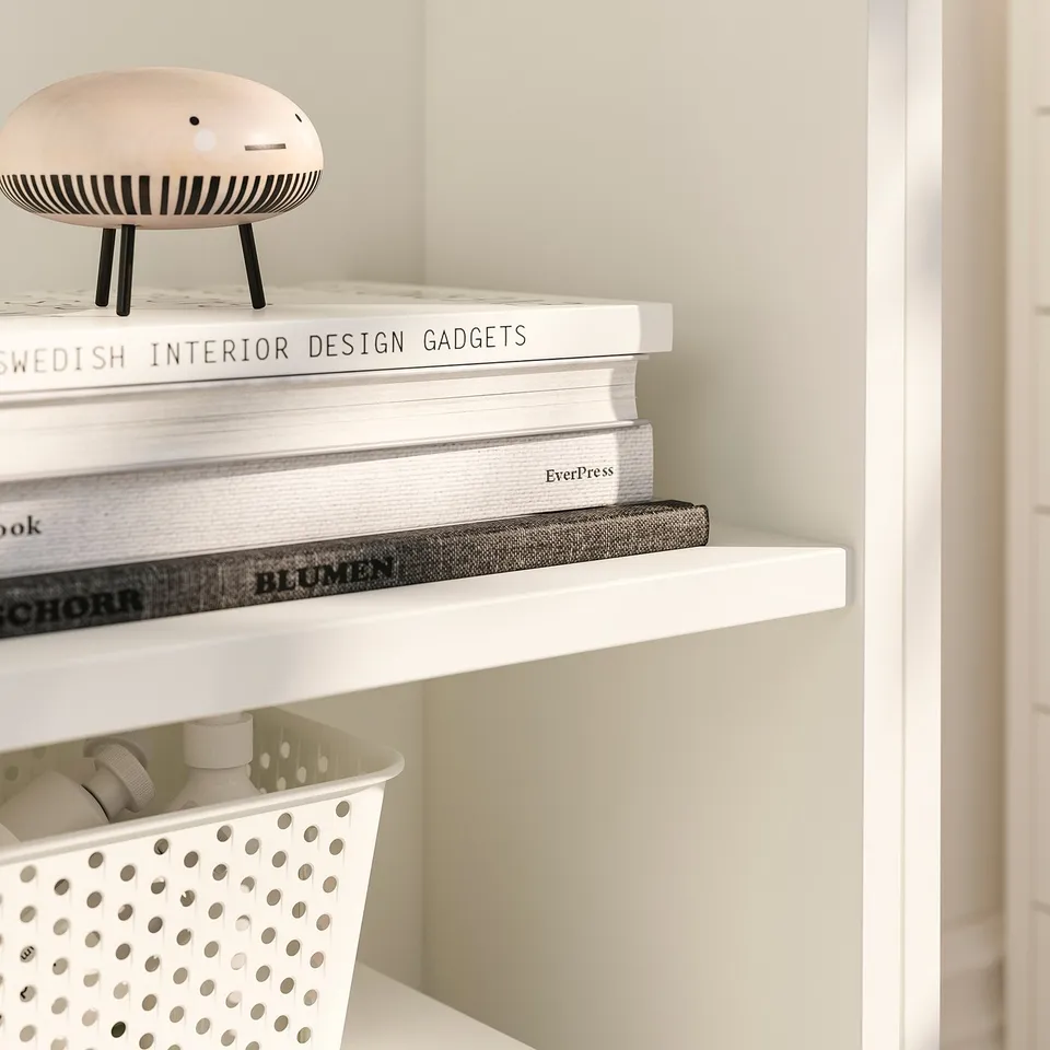 A white BILLY bookcase with sleek, sturdy shelves holding stylish items: a unique decorative piece, stacks of books, and a textured box.