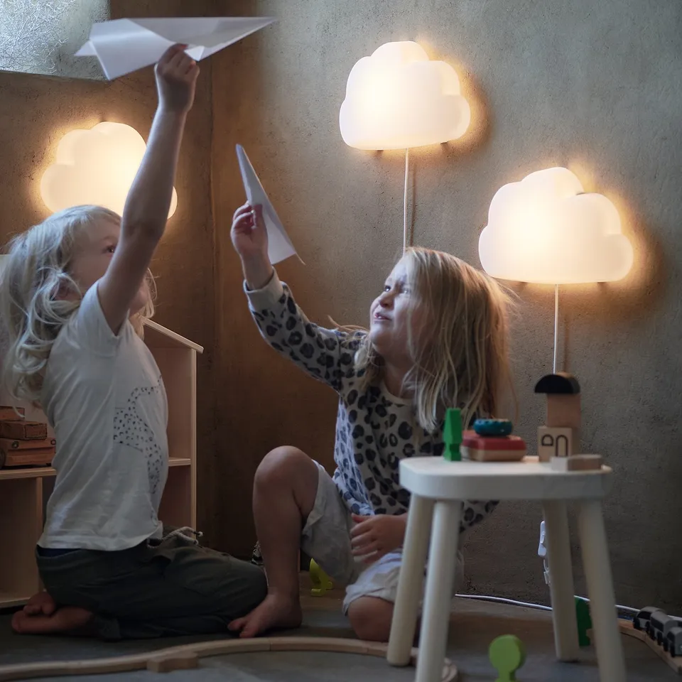 Kids playing with paper planes under eco-friendly cloud lamps.