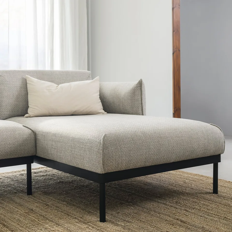 Modern grey sofa with black metal legs and a single white throw pillow.