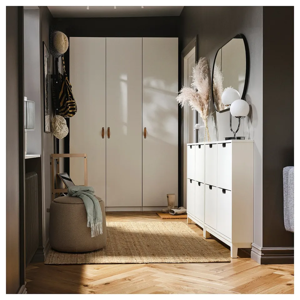 Modern entryway with white storage units, a round ottoman, mirror, and decorations.