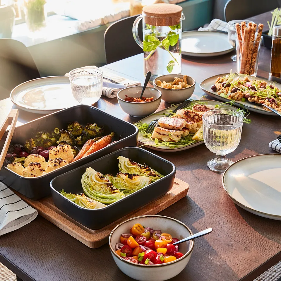 Dining table topped with plates, glasses, and various dishes including vegetables and sauces, set for a meal.