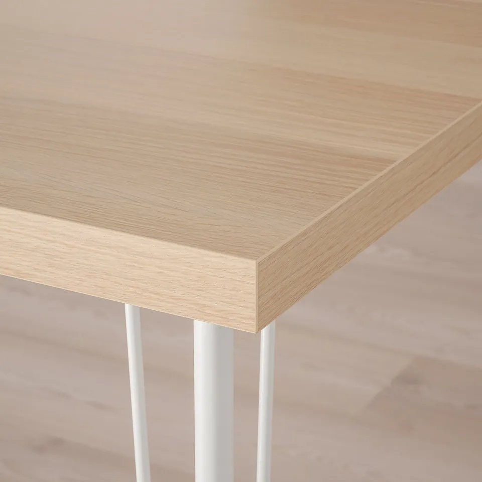 Close-up of light wood tabletop with smooth, even finish and clean, mitered edge, supported by thin metal legs.
