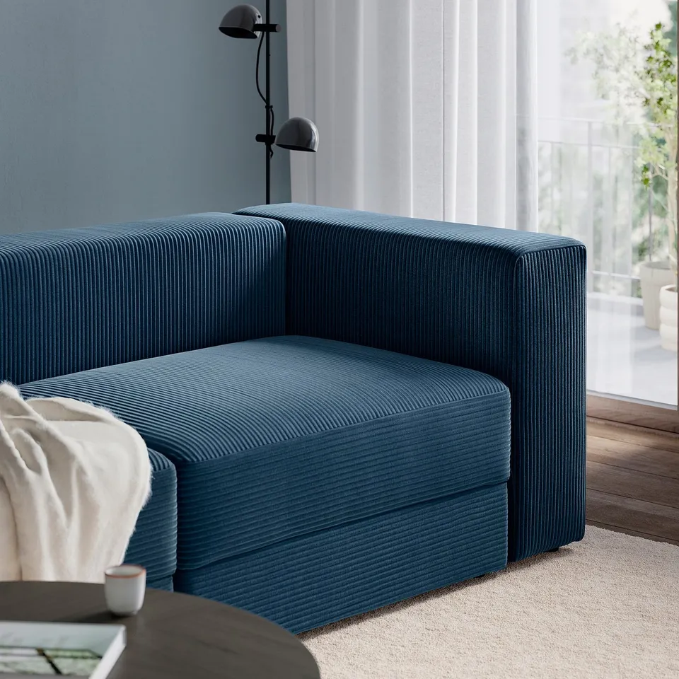 A modern blue JÄTTEBO modular sofa with a stylish, striped cover. A lamp and open window are in the background.