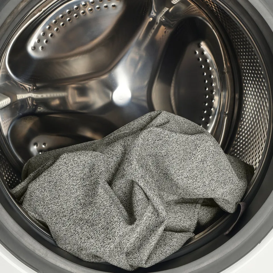 Washing machine interior with crumpled grey garment. Packed drum for washing.