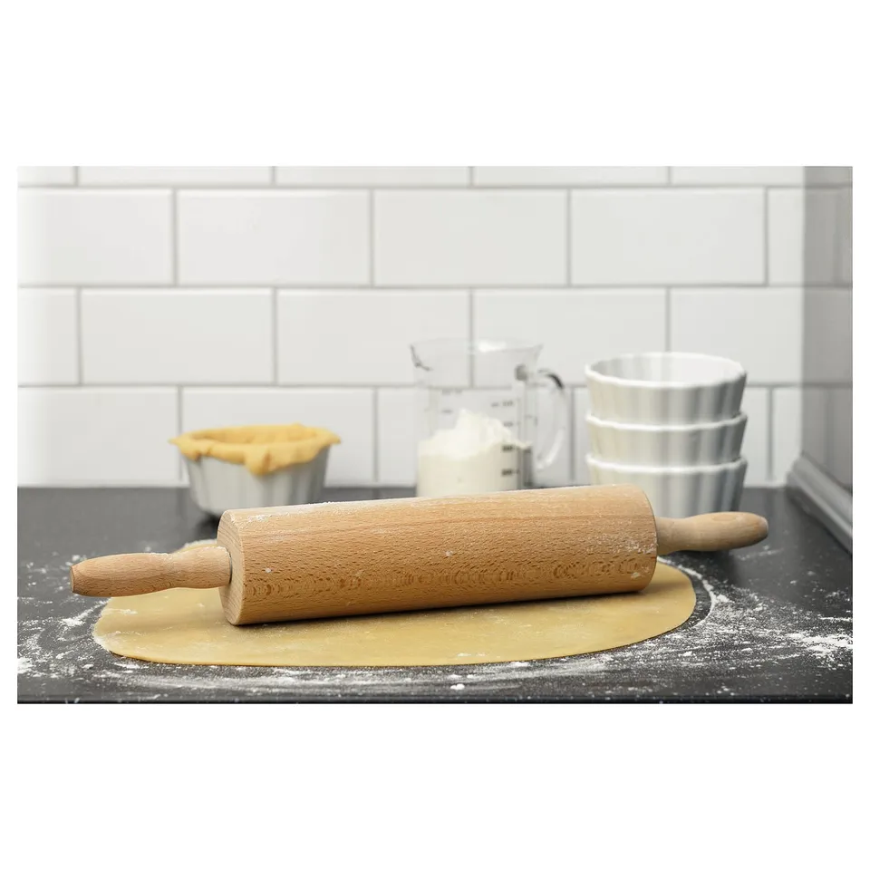 Wooden rolling pin on dough with baking tools near, suitable for rolling out pastry or pizza, set on kitchen counter.